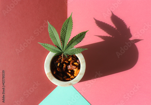 Cannabis plant leaf in a marble pot with a spicy hot red chilly paper, on a flat pink, brown and light blue background. Geometrical minimal spicy food concept.  photo