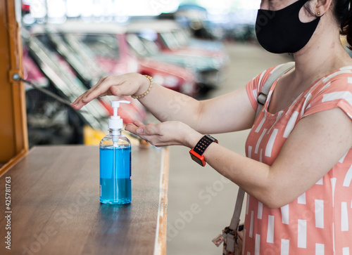 A bussiness woman using alcohol antiseptic gel and wearing prevention mask before starting work to prevent the spread of the corona virus or COVID19.Selective focus at hand. 
