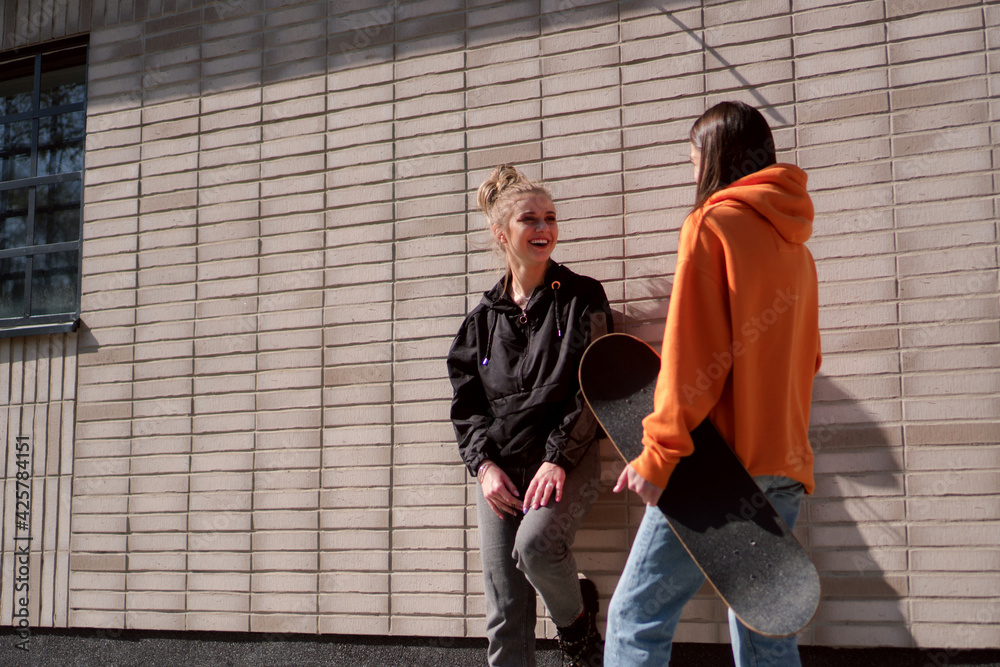 Two teenage skater girls are hanging out in the neighborhood, chatting and smiling. Two teenage skater girls are hanging out in the neighborhood, chatting and smiling.
