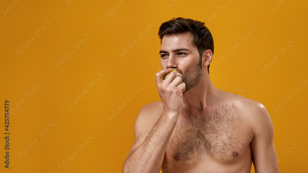 Fototapeta premium Young bearded man with naked torso eating apple
