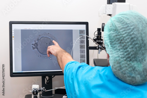 Embryologists perform test with human eggs. Doctor working on manipulator fertilizing human egg in fertility clinic lab, explaining the process, IVF treatment. Artificial insemination clinic. photo