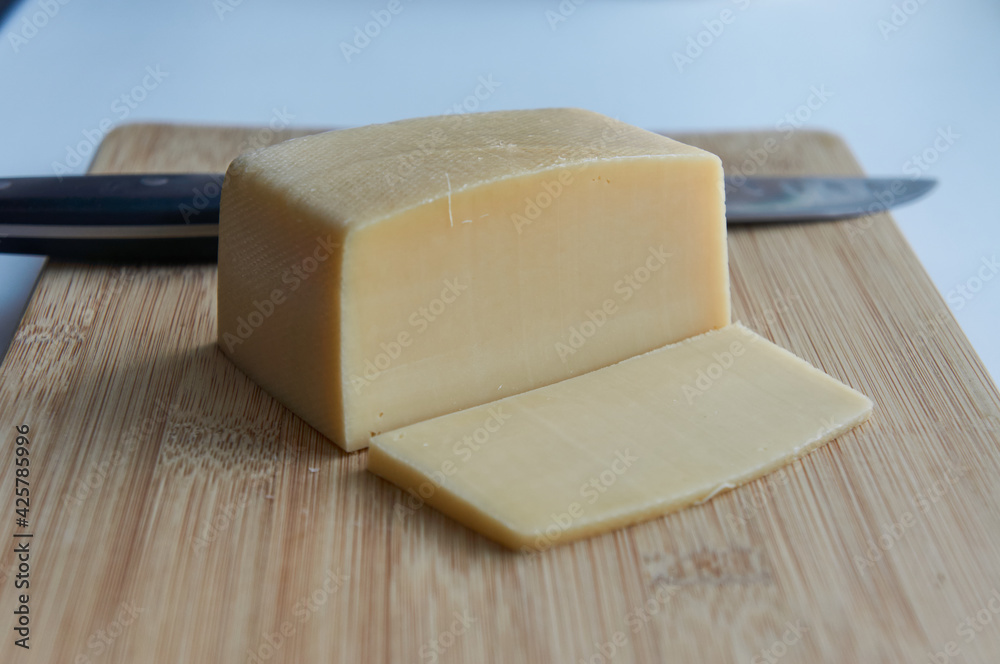 Kitchen iron knife with a slice of cheese and square big piece of cheese on a wooden cutting board