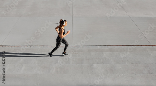 Trendy active fit woman running along arena stand