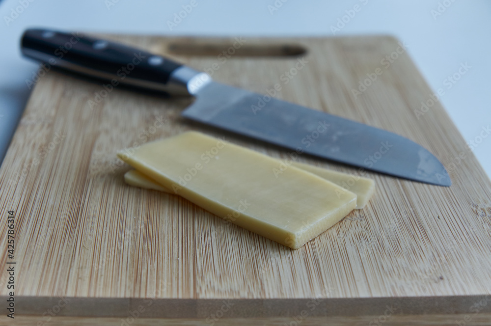 Two slices of cheese with a n iron knife  on a wooden cutting board