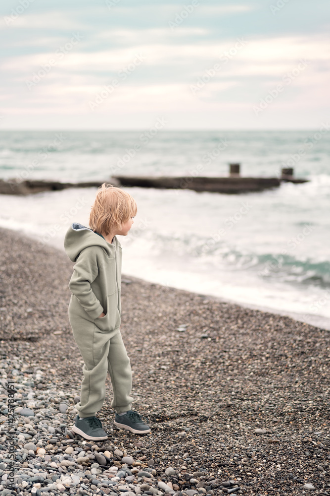 Little cute blonde hair boy walking and playing on the pebble beach Little cute blonde hair boy walking and playing on the pebble beach