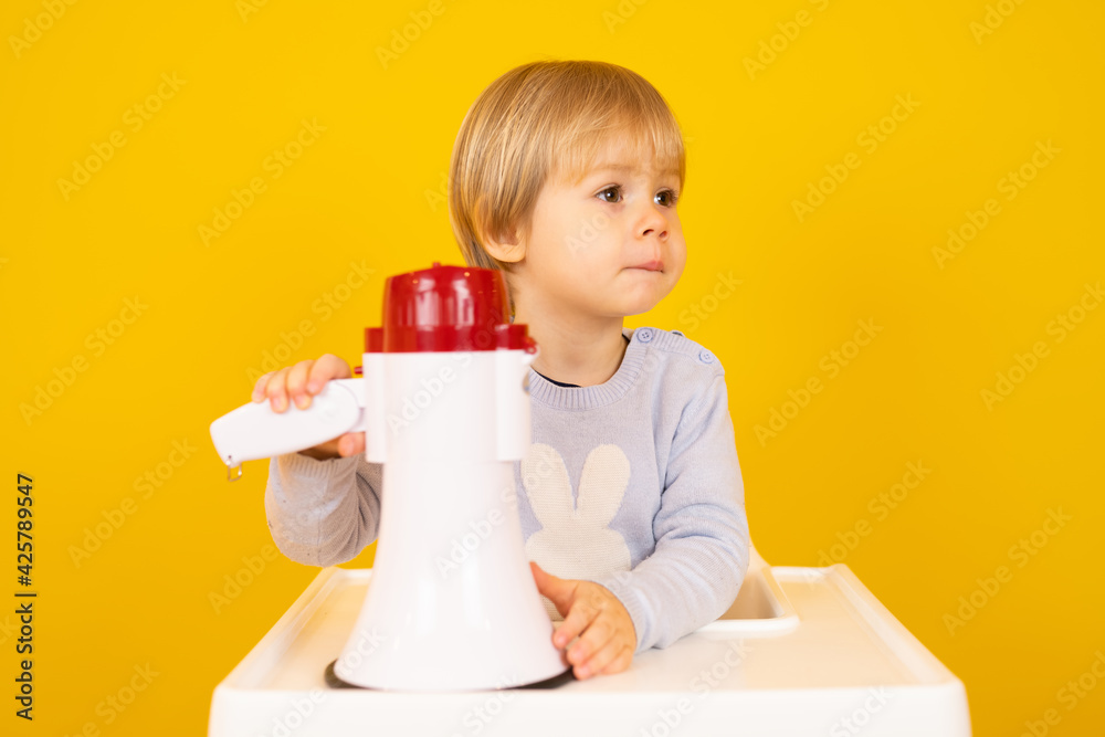 Beautiful smiling boy sitting and holding a megaphone isolated over yellow background. Beautiful smiling boy sitting and holding a megaphone isolated over yellow background.