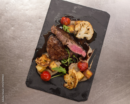 Juicy Beef rump steak from marble beef medium rare with spices and grilled vegetables on black stone plate, close-up.
