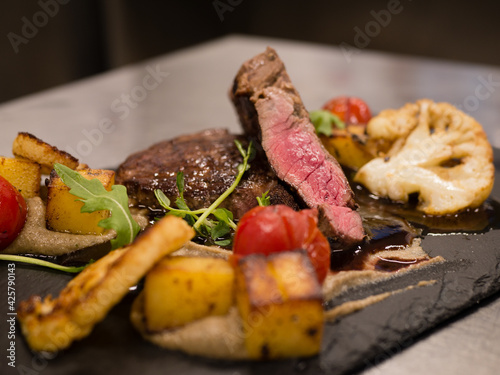 Juicy Beef rump steak from marble beef medium rare with spices and grilled vegetables on black stone plate, close-up.