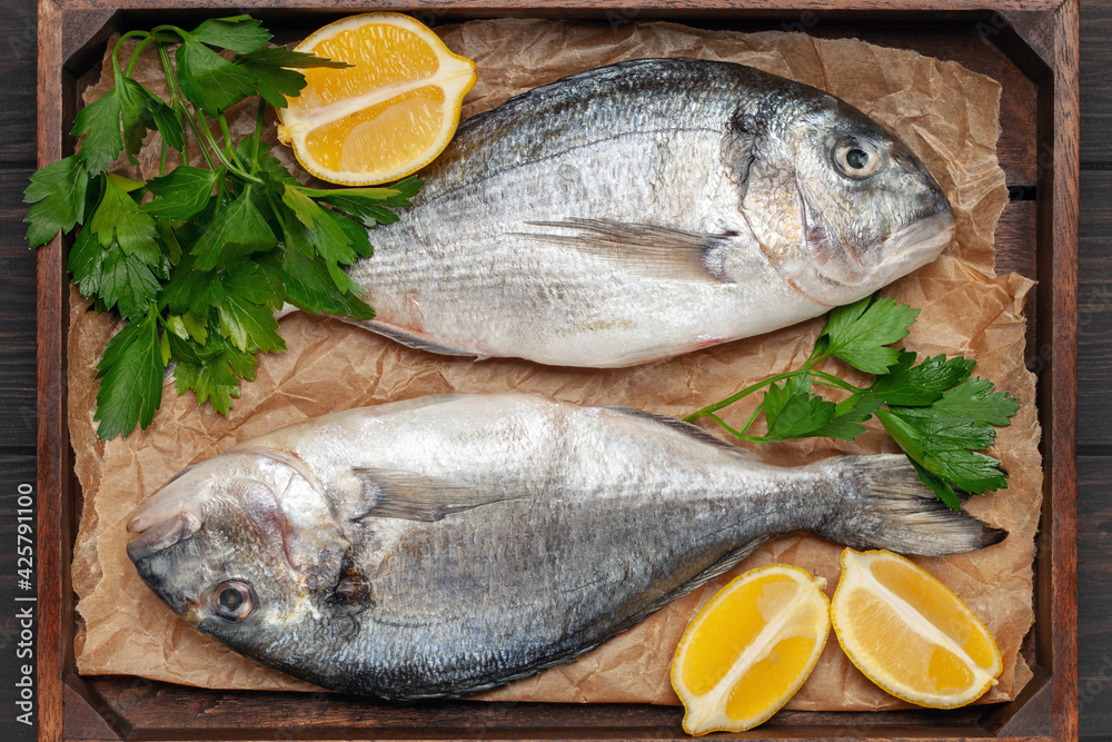 Raw dorado fish with lemon and parsley in a dish on the table. Top View