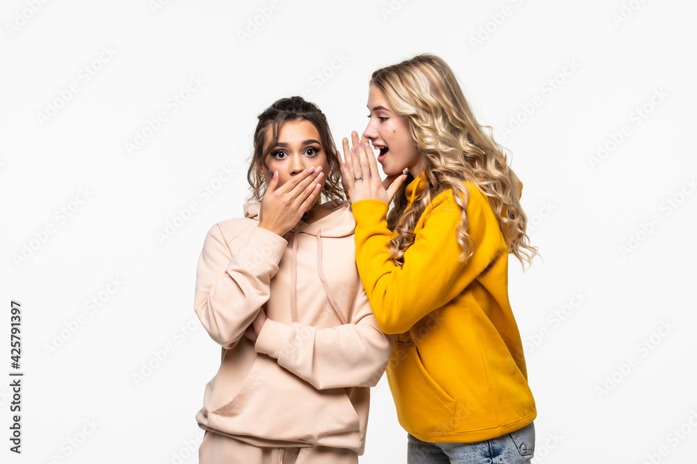 Young woman telling gossip to her girlfriend isolated over gray background Young woman telling gossip to her girlfriend isolated over gray background