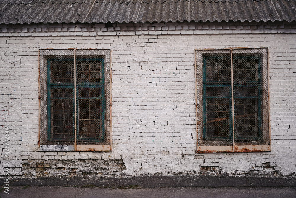 White brick wall of an old building. Two windows closed with bars.
