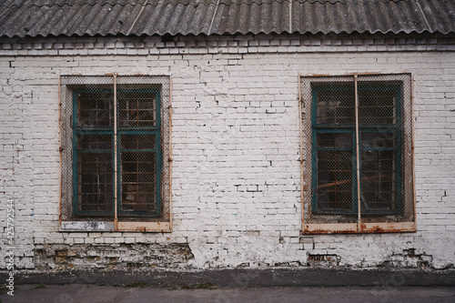 White brick wall of an old building. Two windows closed with bars.