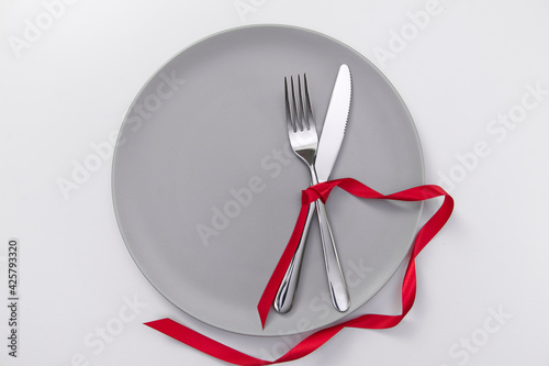 Festive table setting with red ribbon. Fork and knife on a gray plate and card postcard for text. Copy space. High quality photo