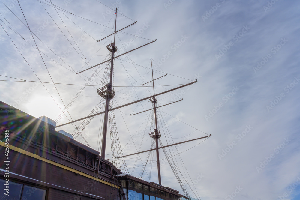 The masts of the ship against the background of the blue and white sky. Close-up. The ship was shot in backlight. Rainbow rays of the sun peek out from the masts of the ship. The masts of the ship against the background of the blue and white sky. Close-up. The ship was shot in backlight. Rainbow rays of the sun peek out from the masts of the ship.