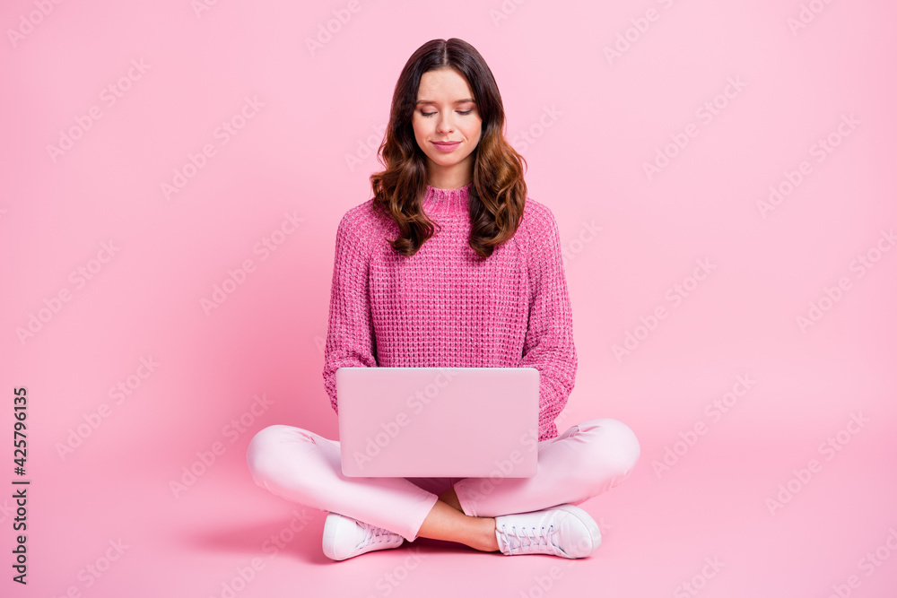 Full size photo of optimistic nice brunette lady sit write laptop wear pink sweater trousers sneakers isolated on pink background Full size photo of optimistic nice brunette lady sit write laptop wear pink sweater trousers sneakers isolated on pink background
