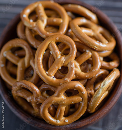 Lot of whole mini salted pretzels stack in a wooden bowl.