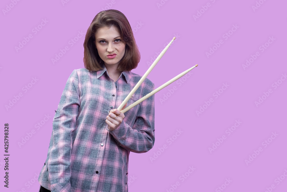 young beautiful girl, musician, holding drum sticks in hands. In a plaid shirt on a pink background young beautiful girl, musician, holding drum sticks in hands. In a plaid shirt on a pink background