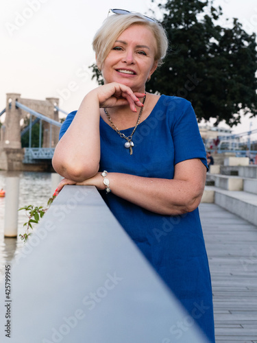 Happy elderly blonde woman in blue dress in summer park.