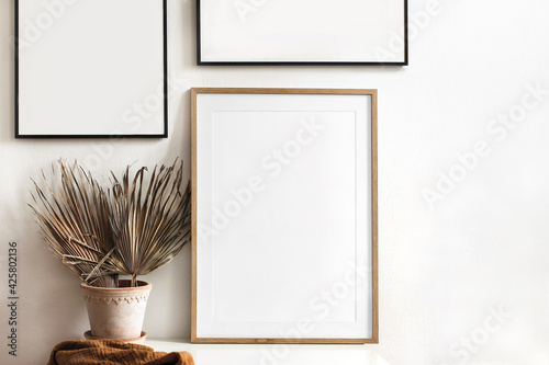 Set of black portrait picture frame mockups. Dry palm leaves in flower pot and rusty linen textile on table. White wall background. Boho exotic interior design. Living room. Neutral color palette.