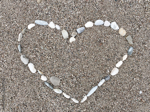 Heart made of sea pebbles on the beach on the sand.  Close up, top view, flat lay, copy space.  Romance, love concept.  Valentine's card.  Sign, symbol of love.