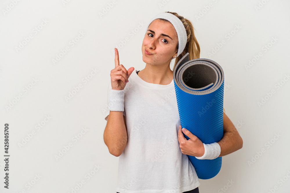 Young sporty woman holding a mat isolated on white background showing number one with finger. Young sporty woman holding a mat isolated on white background showing number one with finger.