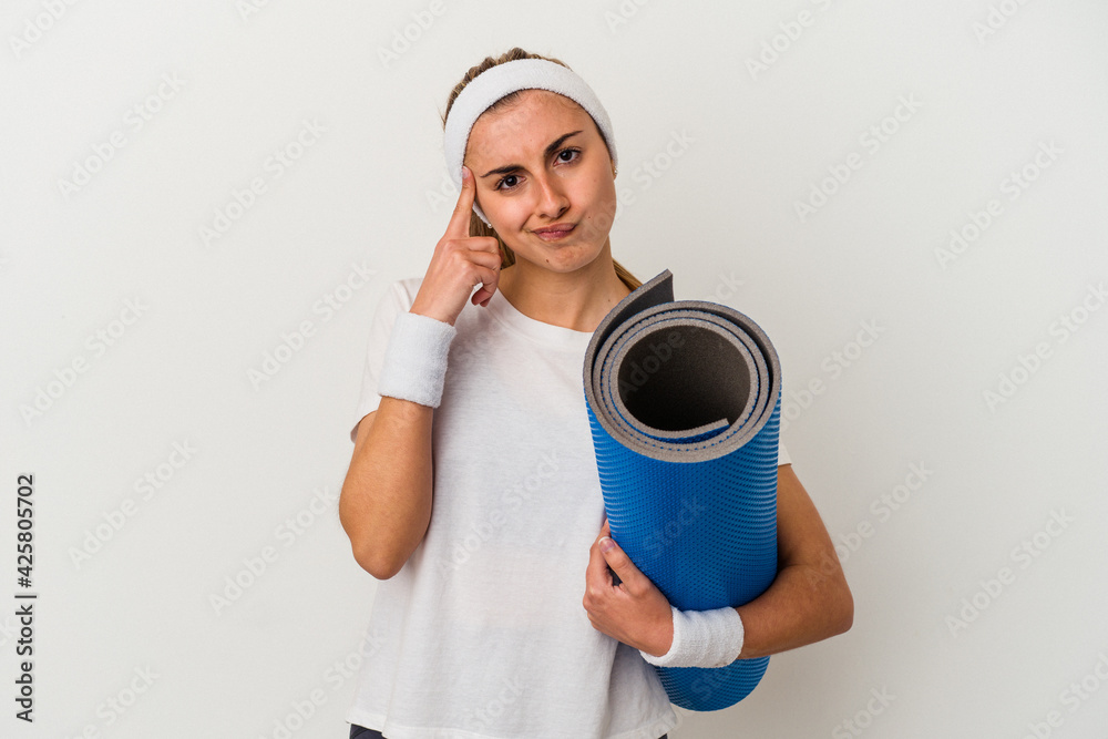 Young sporty woman holding a mat isolated on white background pointing temple with finger, thinking, focused on a task. Young sporty woman holding a mat isolated on white background pointing temple with finger, thinking, focused on a task.
