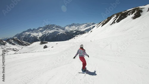 A snowboarding woman in pink outfit going down a perfectly groomed slope of Heiligenblut complex in Austrian Alps. There are high mountain chains around. She is wearing a helmet. Winter madness. 
