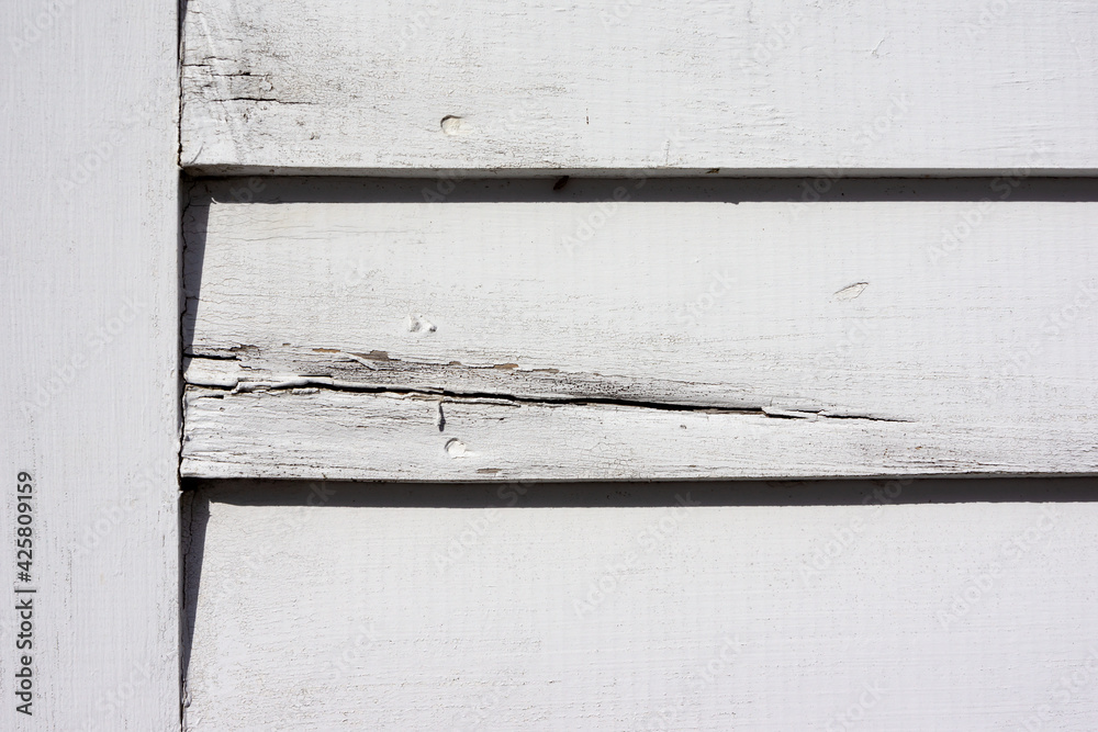 Old clapboard siding painted white next to a trim board showing cracks and wear Old clapboard siding painted white next to a trim board showing cracks and wear