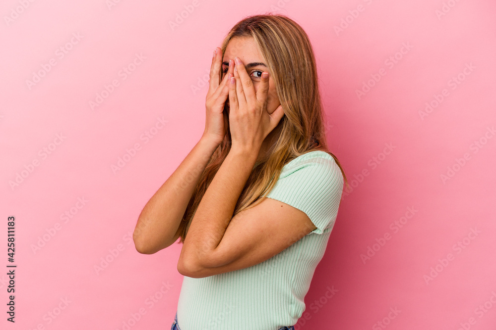 Young blonde caucasian woman isolated on pink background blink through fingers frightened and nervous. Young blonde caucasian woman isolated on pink background blink through fingers frightened and nervous.