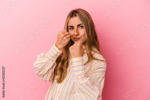 Young blonde caucasian woman isolated on pink background throwing a punch, anger, fighting due to an argument, boxing.