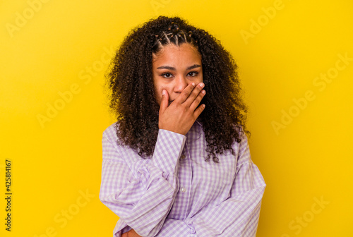 Young african american woman isolated on yellow background covering mouth with hands looking worried.