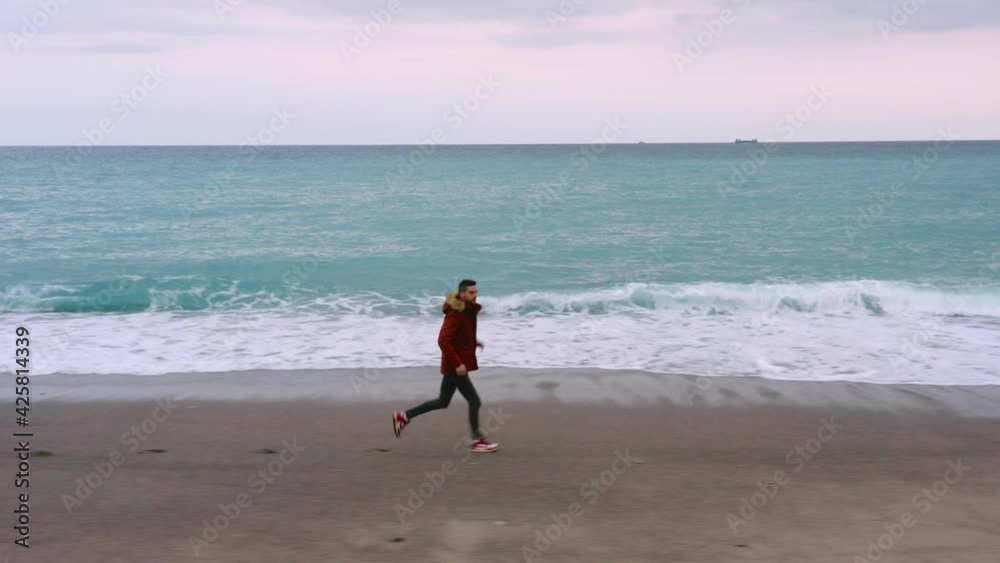 Ragazzo corre vicino al mare sulla spiaggia con cappotto Ragazzo corre vicino al mare sulla spiaggia con cappotto