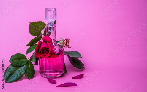 Perfumed rose water in glass bottle. Infused cosmetic toner with flower petals over pink background photo