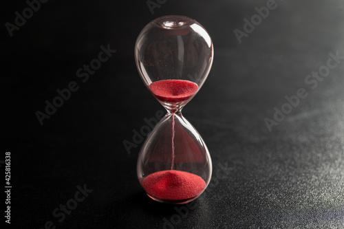 Sand passes through an hourglass, measuring the travel time counting down to the deadline, against a dark background with space for text