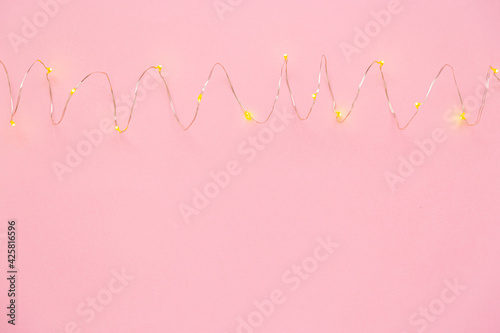 The garland is on. Glowing electric garland on a pink solid background. top view