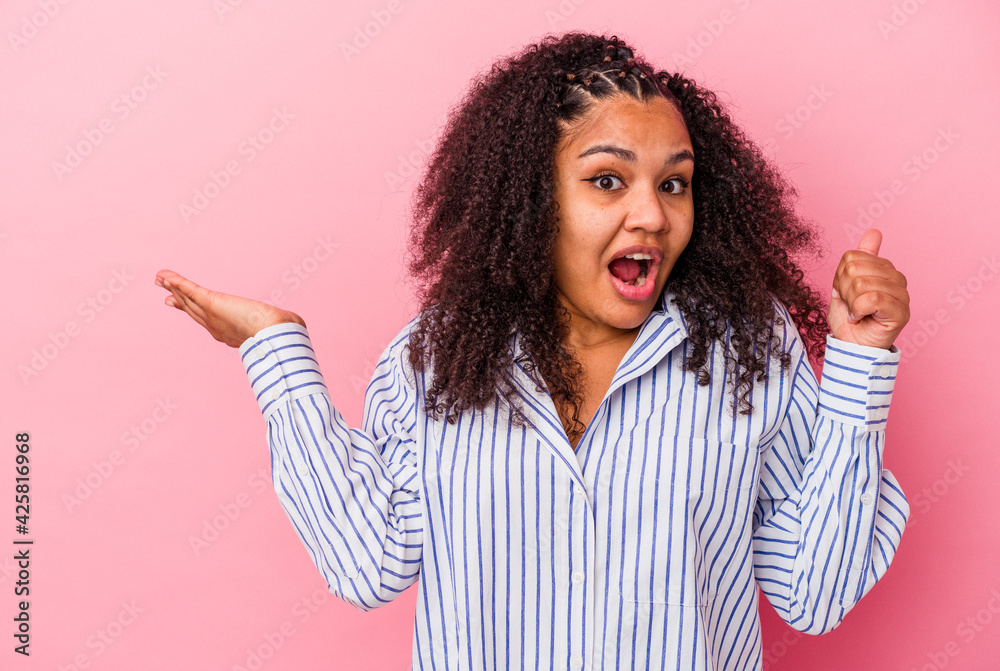 Young african american woman isolated on pink background holds copy space on a palm, keep hand over cheek. Amazed and delighted. Young african american woman isolated on pink background holds copy space on a palm, keep hand over cheek. Amazed and delighted.