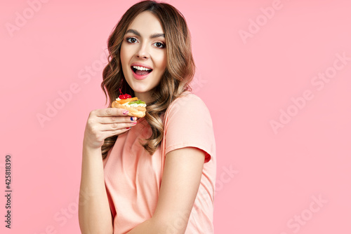 Beautiful smiling young woman with a delicious pastry cake on pink background