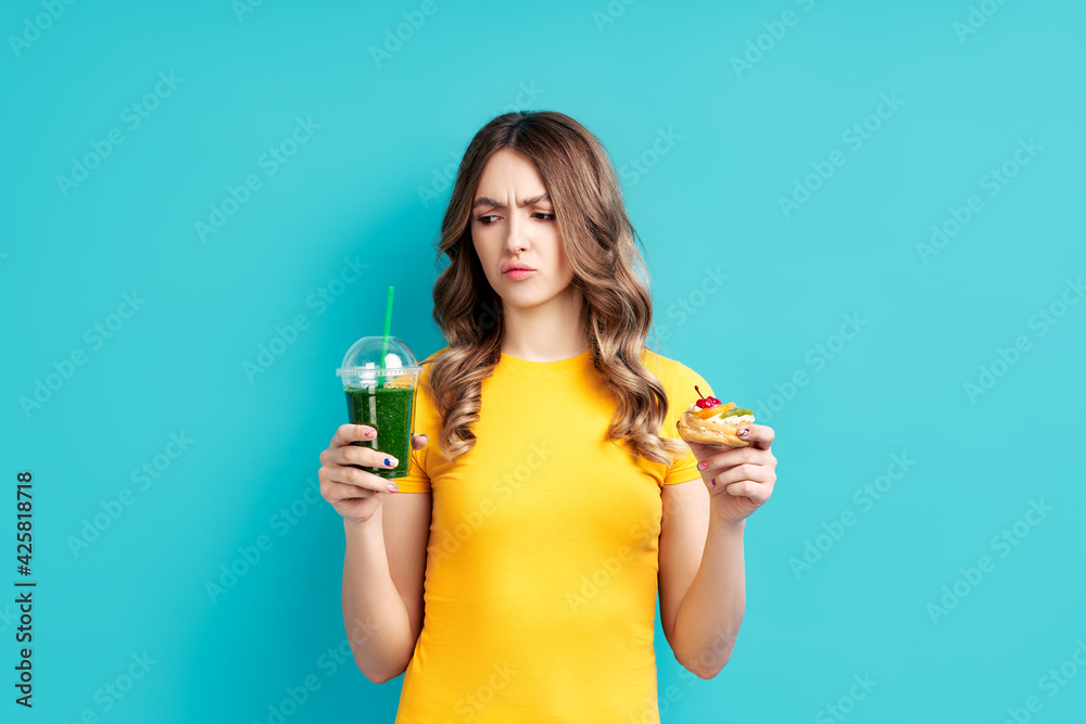 Unhappy woman on dieting looking to smoothie choosing between detox juice and sweets Unhappy woman on dieting looking to smoothie choosing between detox juice and sweets