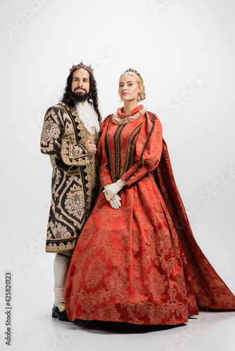 full length of historical interracial couple in crowns and medieval clothing on white