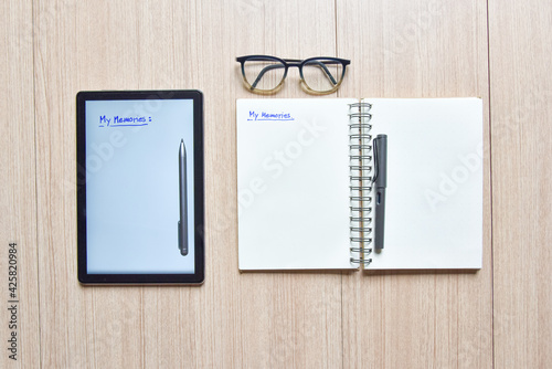 a tablet and notebook with pens and eyeglasses on wood table,old and new style of technology to note and take a memo for note or lists concept