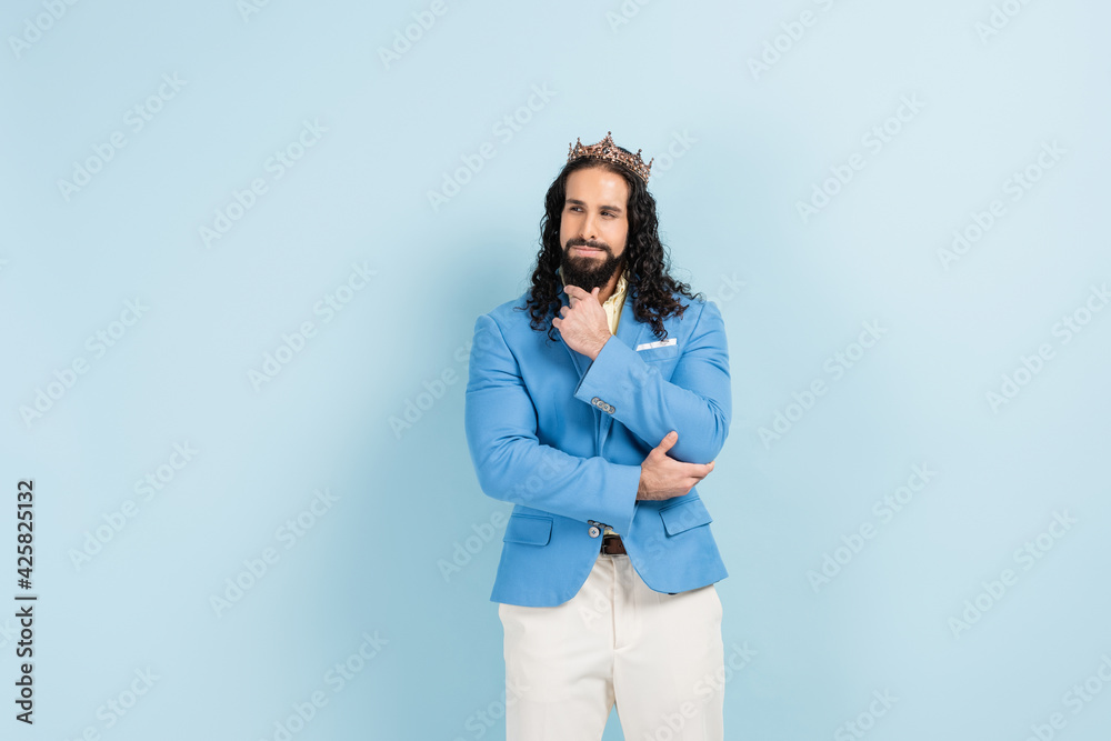 pensive and bearded hispanic man in crown and jacket posing on blue pensive and bearded hispanic man in crown and jacket posing on blue