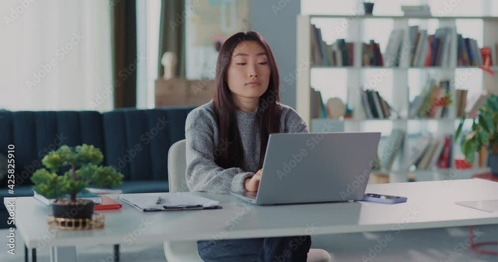 Cheerful young asian woman finishing project before deadline, resting in chair and looking proudly on laptop monitor. Successful freelancer.