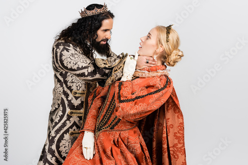 cruel hispanic king in medieval clothing choking shocked queen in golden crown isolated on white