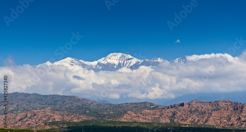 Scenic view of snow capped peak El Plata (6100 MSL) above the clouds, as seen from Lake Potrerillos, in Mendoza, Argentina.