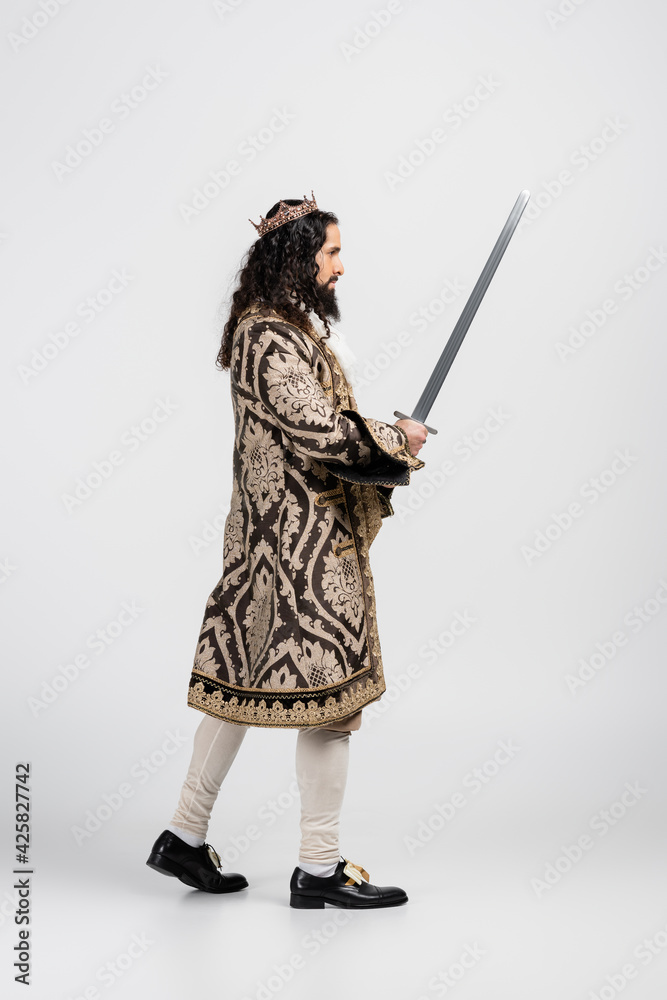 side view of hispanic king in medieval clothing and crown holding sword on white side view of hispanic king in medieval clothing and crown holding sword on white