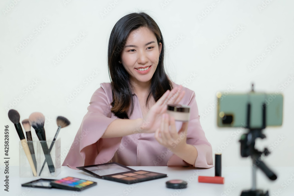 An Asian blogger beauty blogger shooting a video of herself wearing an orange lipstick in a studio. An Asian blogger beauty blogger shooting a video of herself wearing an orange lipstick in a studio.