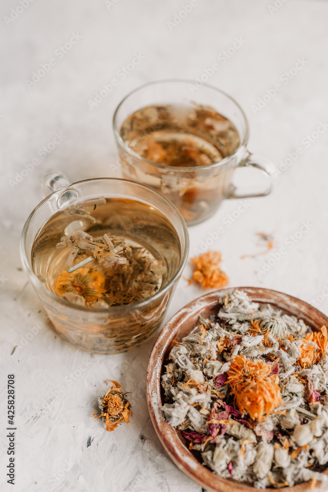 Herbal tea is brewed in glass cups on a light background. Herbal tea ingredients. Dried calendula, mint, Damascus rose, lemon balm, thyme, lavender, lemongrass. Herbal tea is brewed in glass cups on a light background. Herbal tea ingredients. Dried calendula, mint, Damascus rose, lemon balm, thyme, lavender, lemongrass.
