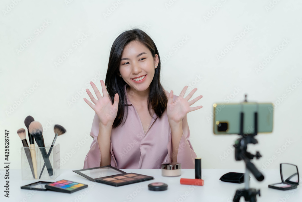 An Asian blogger beauty blogger shooting a video of herself wearing an orange lipstick in a studio. An Asian blogger beauty blogger shooting a video of herself wearing an orange lipstick in a studio.