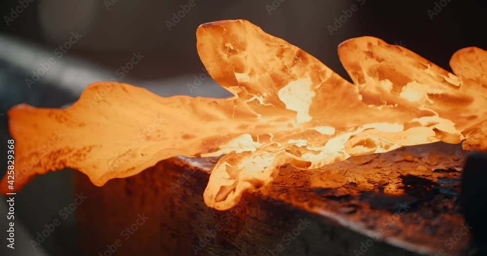 Blacksmith shapes the red hot decorative metal product with hammer on ...