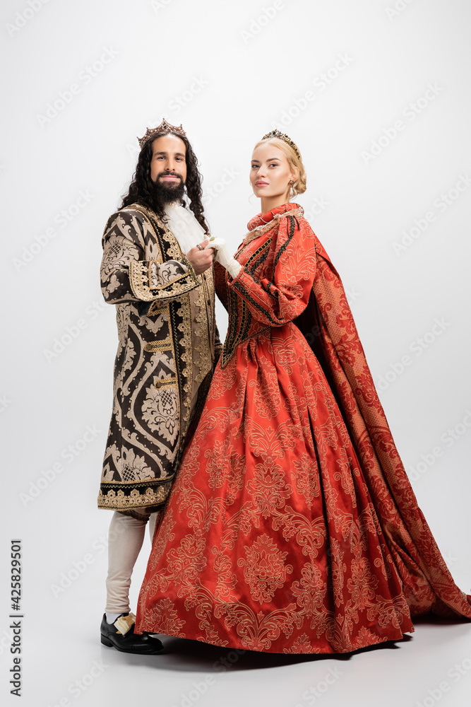 full length of historical interracial couple in royal crowns and medieval clothing on white